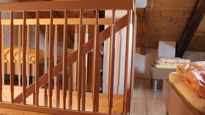 Una culla in legno in una stanza con soffitto spiovente, una sedia bianca e un letto con coperta bianca e arancione.