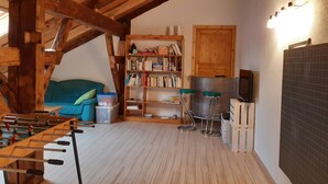 Una stanza accogliente con soffitto in legno, un divano, una libreria, uno sgabello da bar e un televisore.