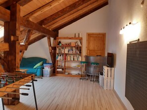 Een gezellige kamer met een houten plafond, een bank, een boekenkast, een barkruk en een televisietoestel.