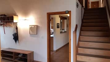 A wooden staircase leading to a second floor, a hallway with a bench and a coat rack, and a kitchen visible through an open doorway.