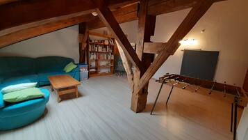 A loft-style room with a wooden ceiling, a blue sofa, a small wooden table, a bookshelf, and a foosball table.