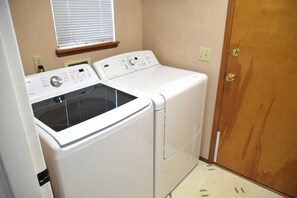 A laundry room with two white washers and dryers, a wooden door, and a window with blinds. - 3-bedroom house in wonderful Federal Way with AC for relaxing stays (Federal Way)