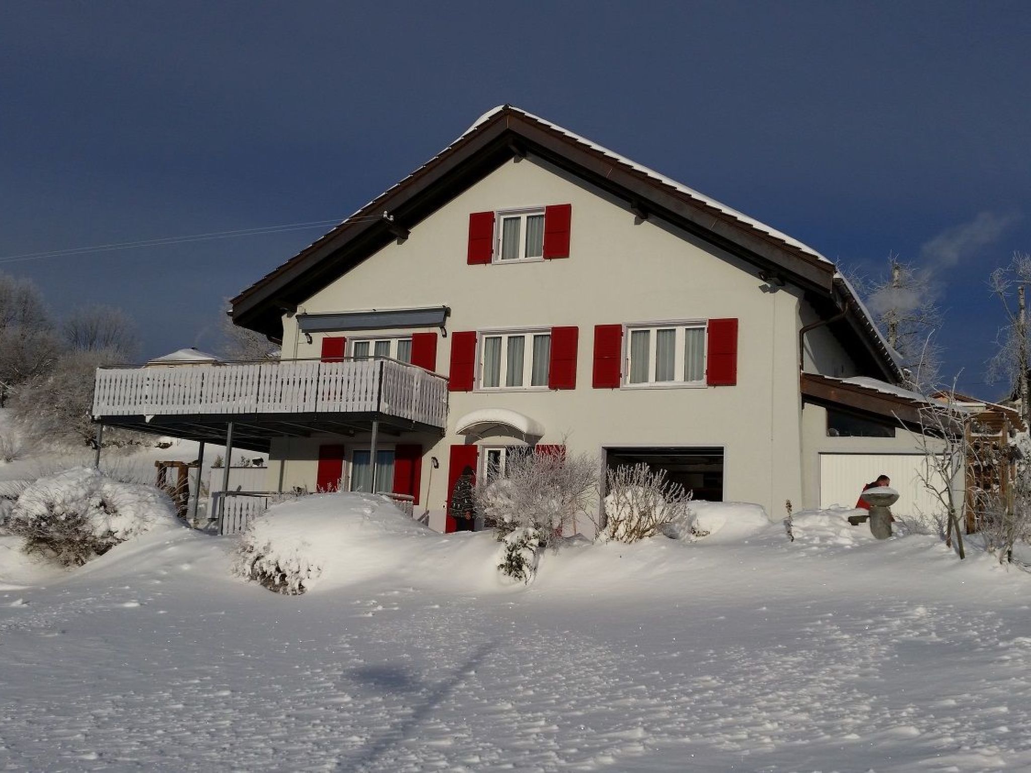 Una casa de dos pisos con balcón, rodeada de nieve.