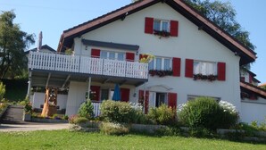 Ein zweistöckiges Gebäude mit Balkon, Treppe und einem Garten.