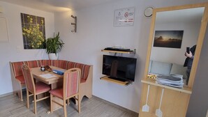 Ein gemütlicher Wohnraum mit Esstisch, Stühlen, Fernseher, Spiegel und einer Zimmerpflanze.