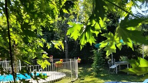 Ein Garten mit Schwimmbad, umzäunter Terrasse und Rasen mit Liegestühlen.