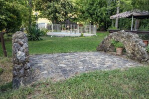 Un sendero de piedra lleva a un área cercada con una piscina, rodeada de follaje y un pabellón.