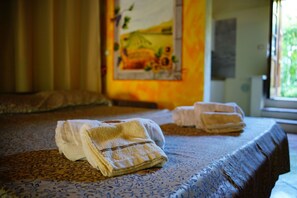 Quarto de hotel com cama, duas toalhas, colcha estampada, um quadro na parede e uma janela.