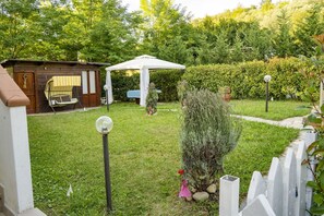 Um jardim com um gazebo, uma cabana de madeira e uma cerca branca.