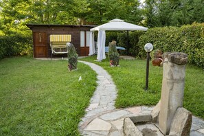 Un sendero de piedra que conduce a una cabaña de madera con un toldo blanco, rodeada de vegetación.