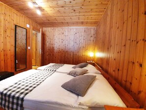 A wooden-paneled room with a bed, pillows, a nightstand, and a mirror. - Bergdohle, (Randa), by Interhome (Randa)