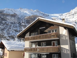 Un edificio de varios pisos con un letrero que dice 'BERGDÖHLE' en el piso superior, rodeado de montañas cubiertas de nieve.