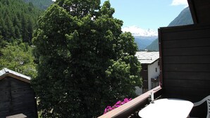 Uma varanda com mesa e cadeiras, cerca de madeira e uma árvore grande.
