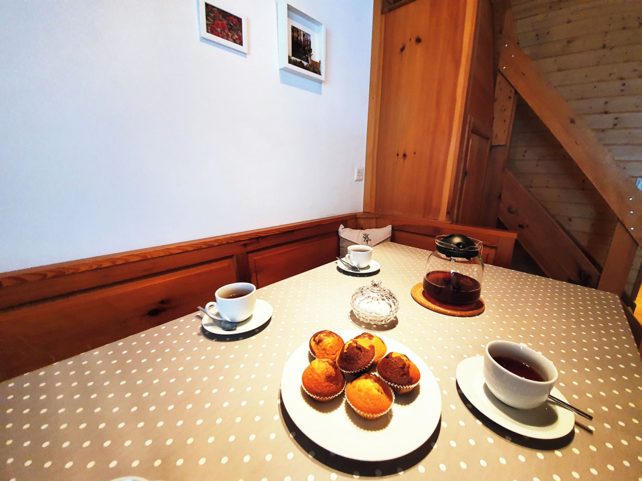 Une table à manger recouverte d’une nappe à pois, une théière, une tasse de thé, une assiette de muffins et une tasse de café.