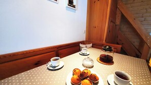 Uma mesa de jantar com toalha quadriculada, um bule de chá, uma xícara de chá, um prato com muffins e uma xícara de café.