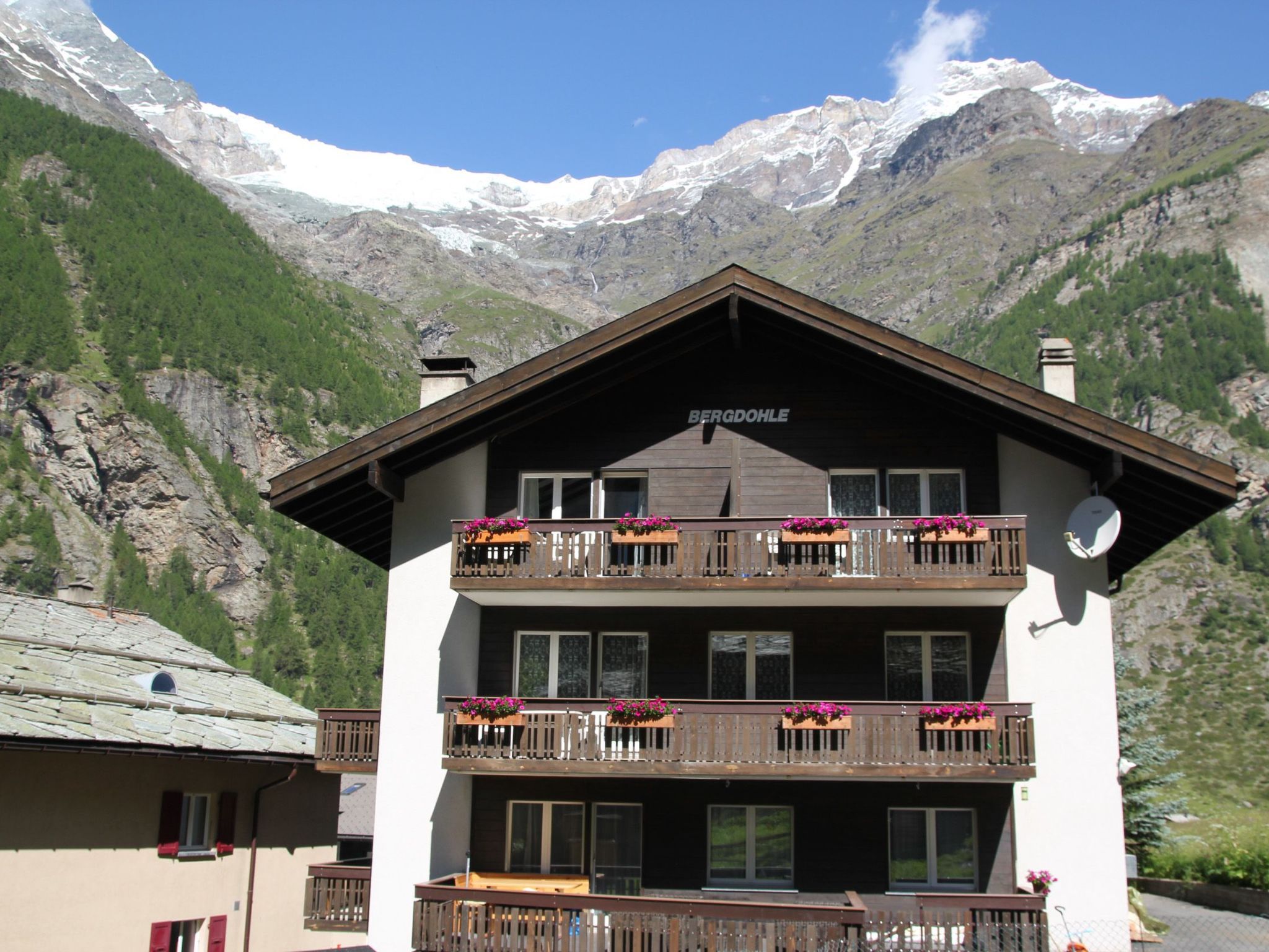 A multi-story building with balconies, a sign reading 'BERGDOLLE,' and a mountainous backdrop.