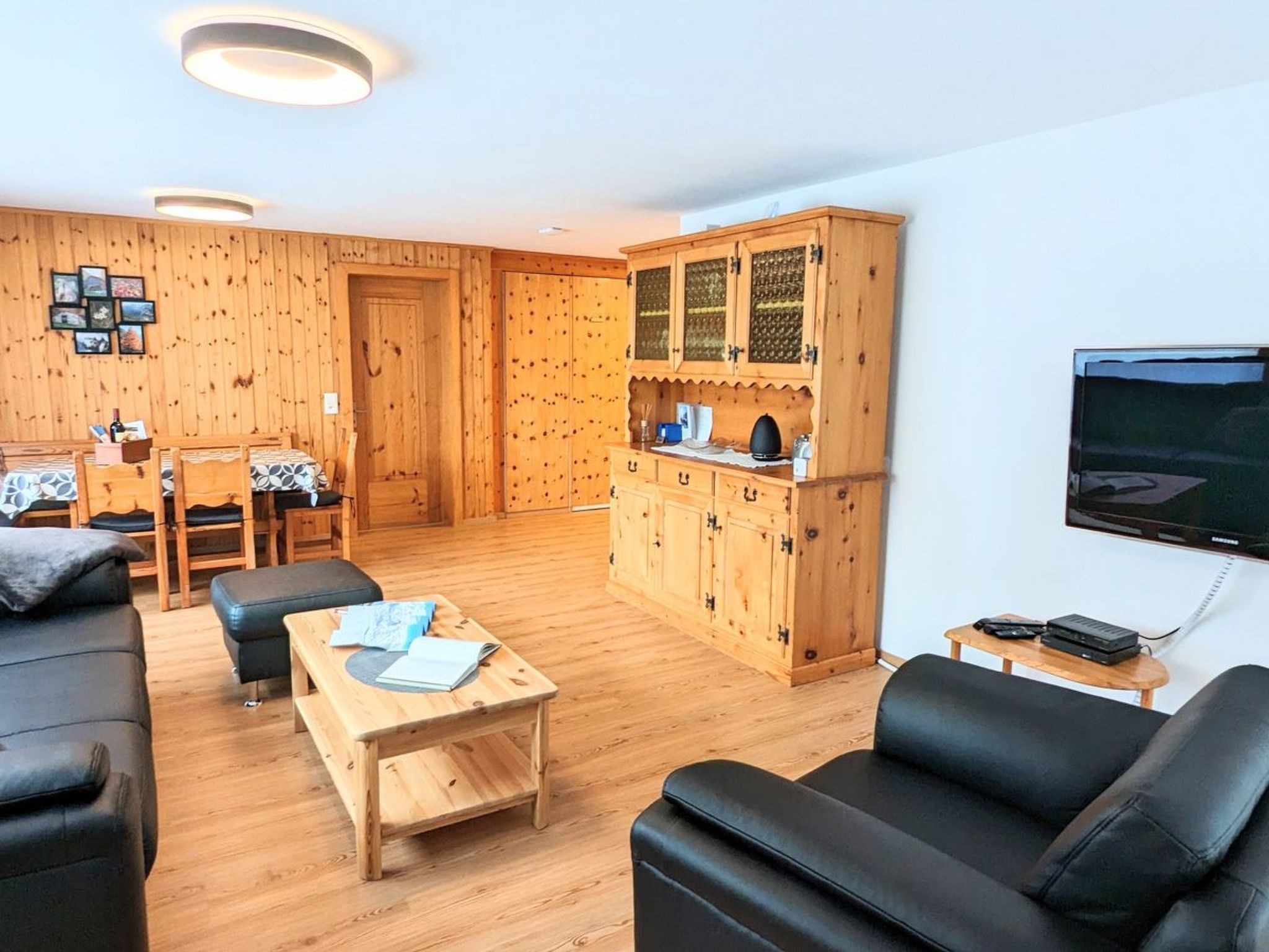 Un salon chaleureux avec un plancher en bois, un canapé en cuir noir, une table basse en bois et un téléviseur fixé au mur.