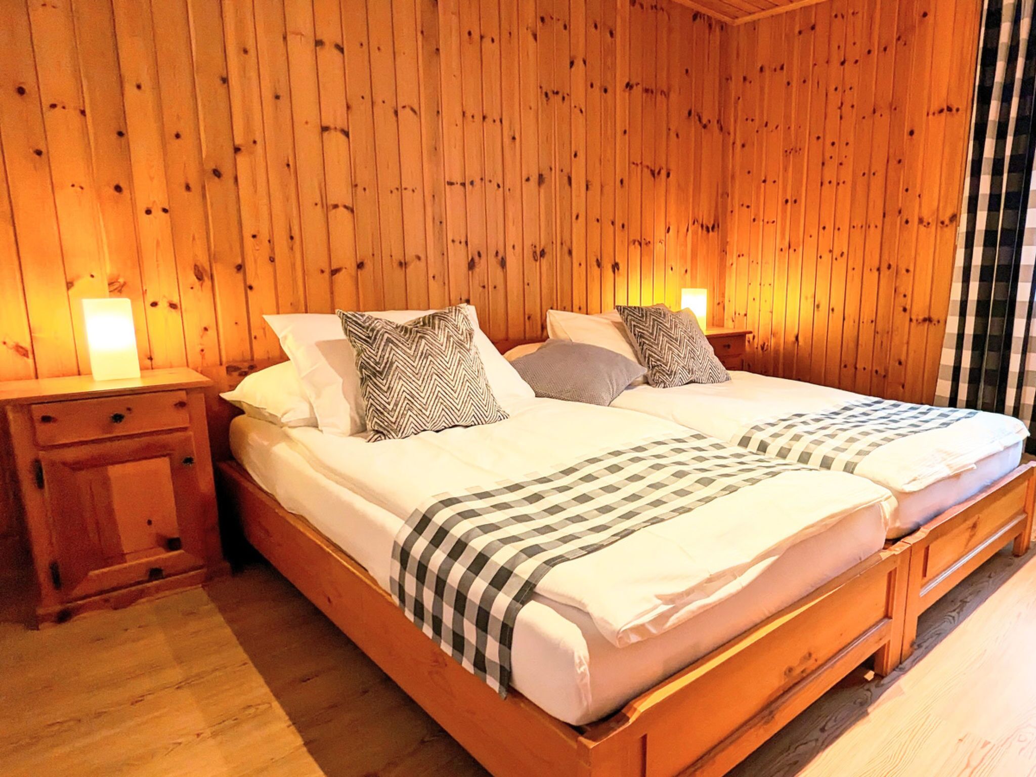 Un lit double avec une couvre-lit à carreaux, deux oreillers, une table de chevet et un mur en bois.