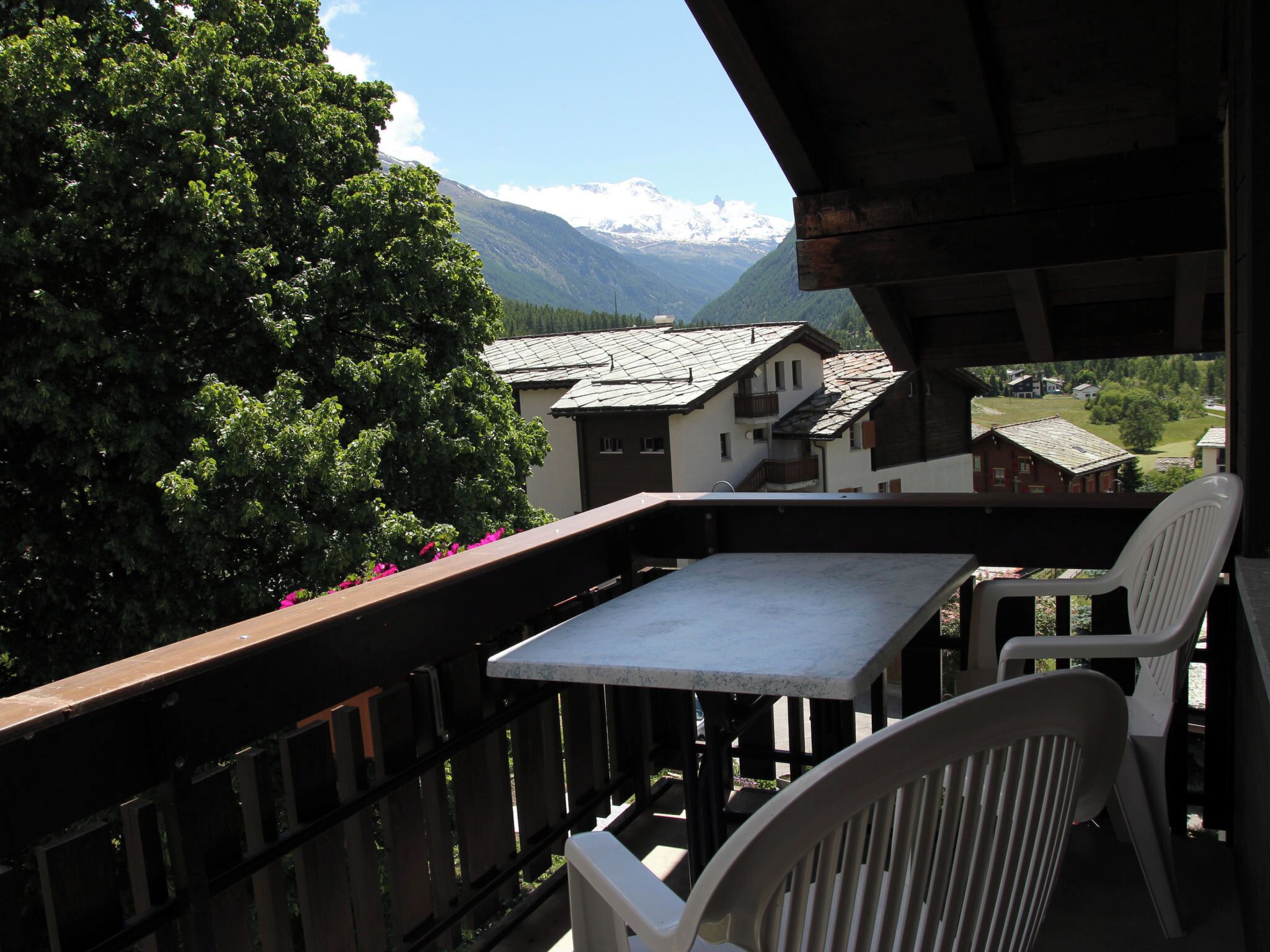 Un balcon avec une table et des chaises, donnant sur un paysage montagneux parsemé de maisons.
