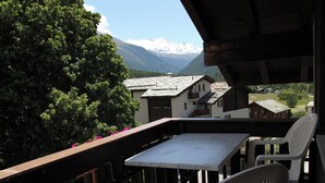 Un balcón con mesa y sillas, con vistas a un paisaje montañoso con casas.