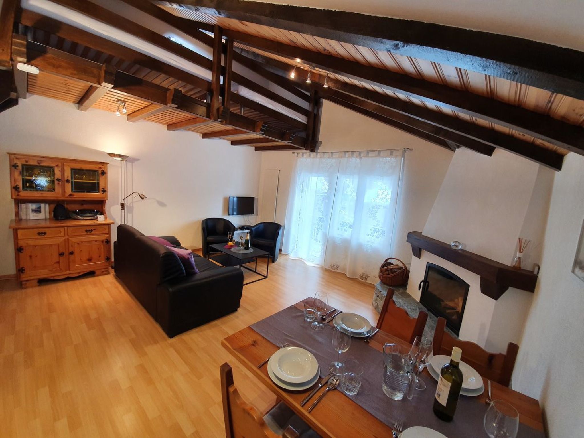Un salon chaleureux avec un plafond en bois, une table à manger dressée pour deux personnes et une cheminée.