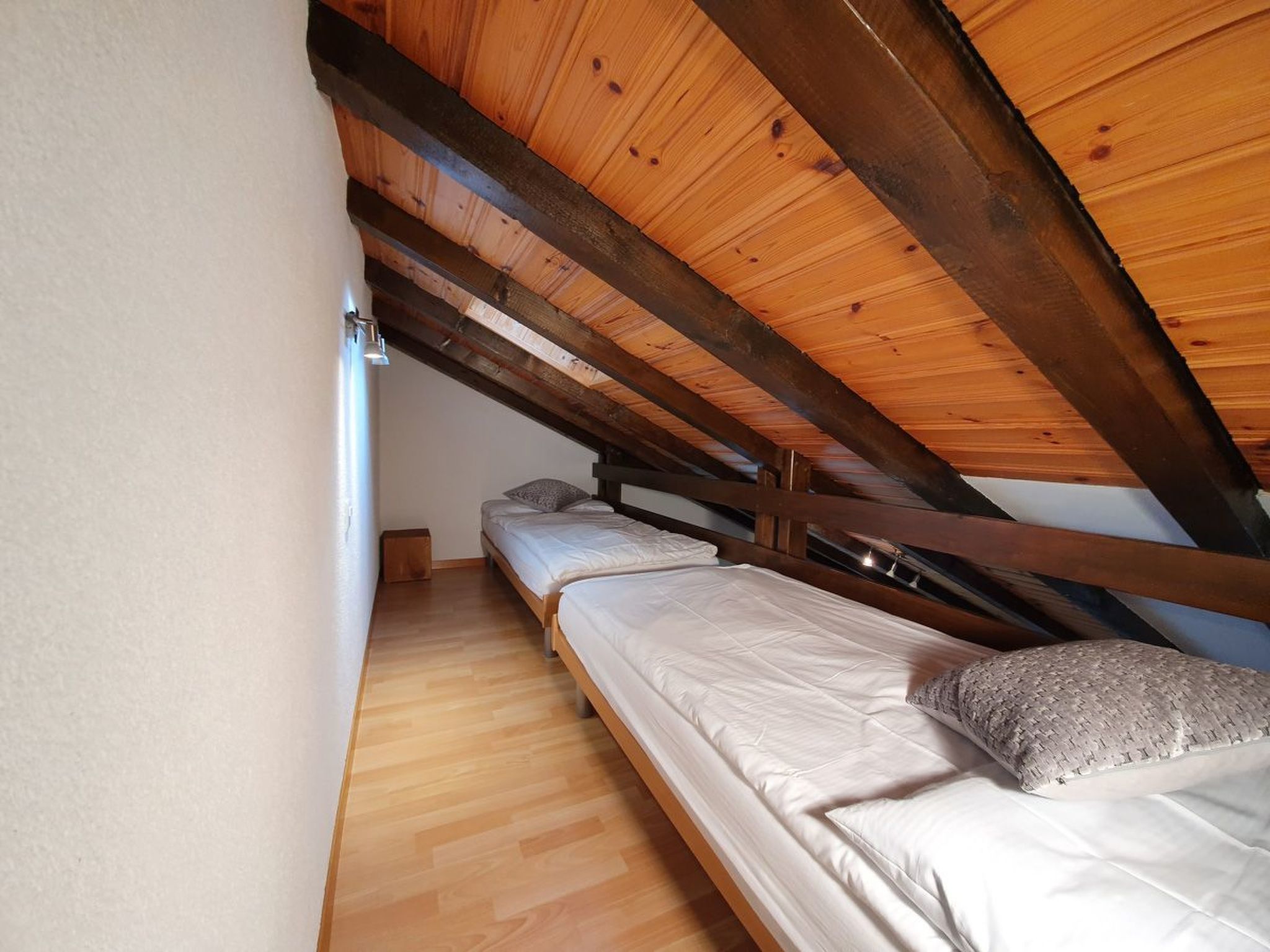Une petite chambre mansardée avec des poutres en bois, deux lits et une petite fenêtre.