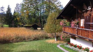Una baita in legno con un balcone, circondata da un prato curato e piante fiorite.