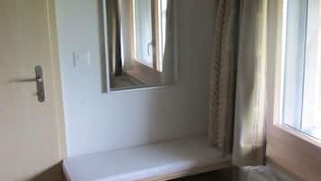 Une pièce avec un banc intégré, un miroir, un radiateur et une fenêtre avec des rideaux.