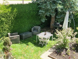 Un patio jardín con mobiliario exterior, una parrilla y un seto.