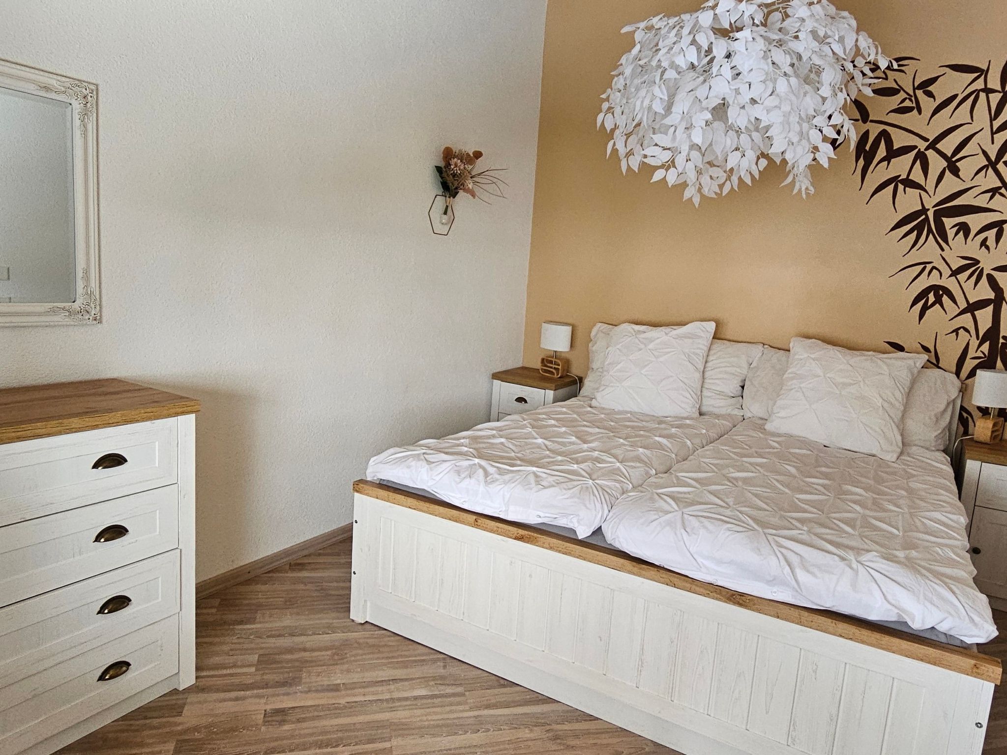Un dormitorio con cama, mesita de noche, lámpara, cómoda y lámpara de pared.