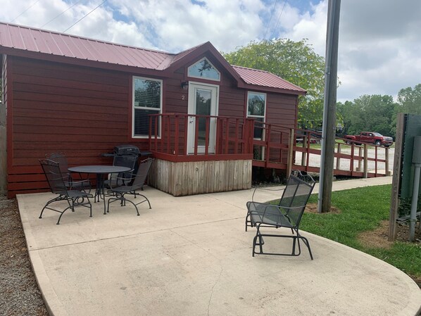 A red wooden building with a covered patio area, outdoor seating, and a visible garage door.