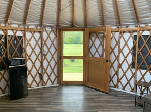 A yurt interior with a wooden door leading to an outdoor area, a small table, and a trash bin.