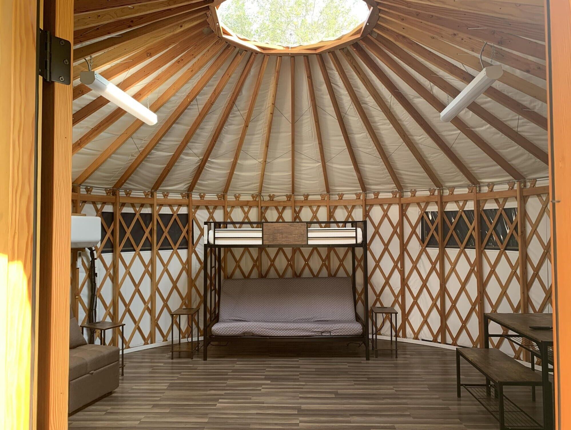A yurt with a central bed, wooden lattice walls, and a wooden floor.