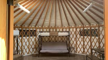 A yurt with a central bed, wooden lattice walls, and a wooden floor.