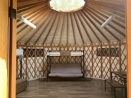 Una yurtas con una cama en el centro, paredes de entramado de madera y suelo de madera.