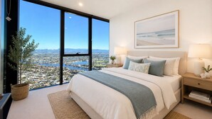 Un dormitorio con un ventanal grande, una cama con almohadas, una mesita de noche con lámpara y un cuadro en la pared.