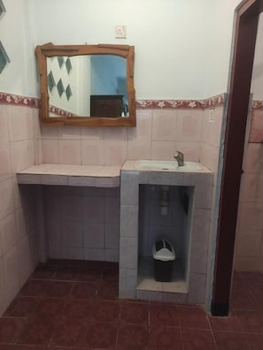 Un baño con lavamanos, espejo y un pequeño cubo de basura.