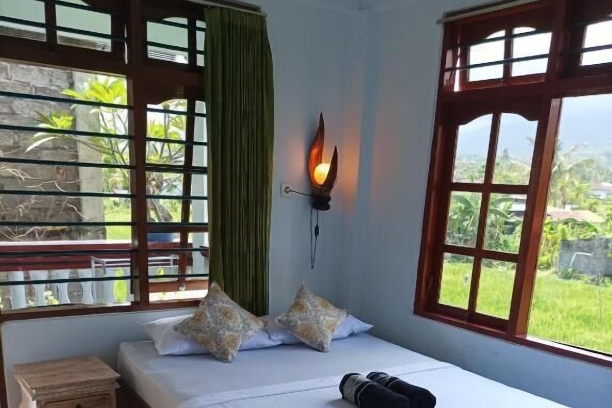 Una cama individual con una colcha blanca, dos almohadas decorativas, una mesita de noche y una lámpara de pared.