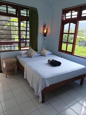 Una cama individual con una colcha blanca, dos almohadas decorativas, una mesita de noche y una lámpara de pared.