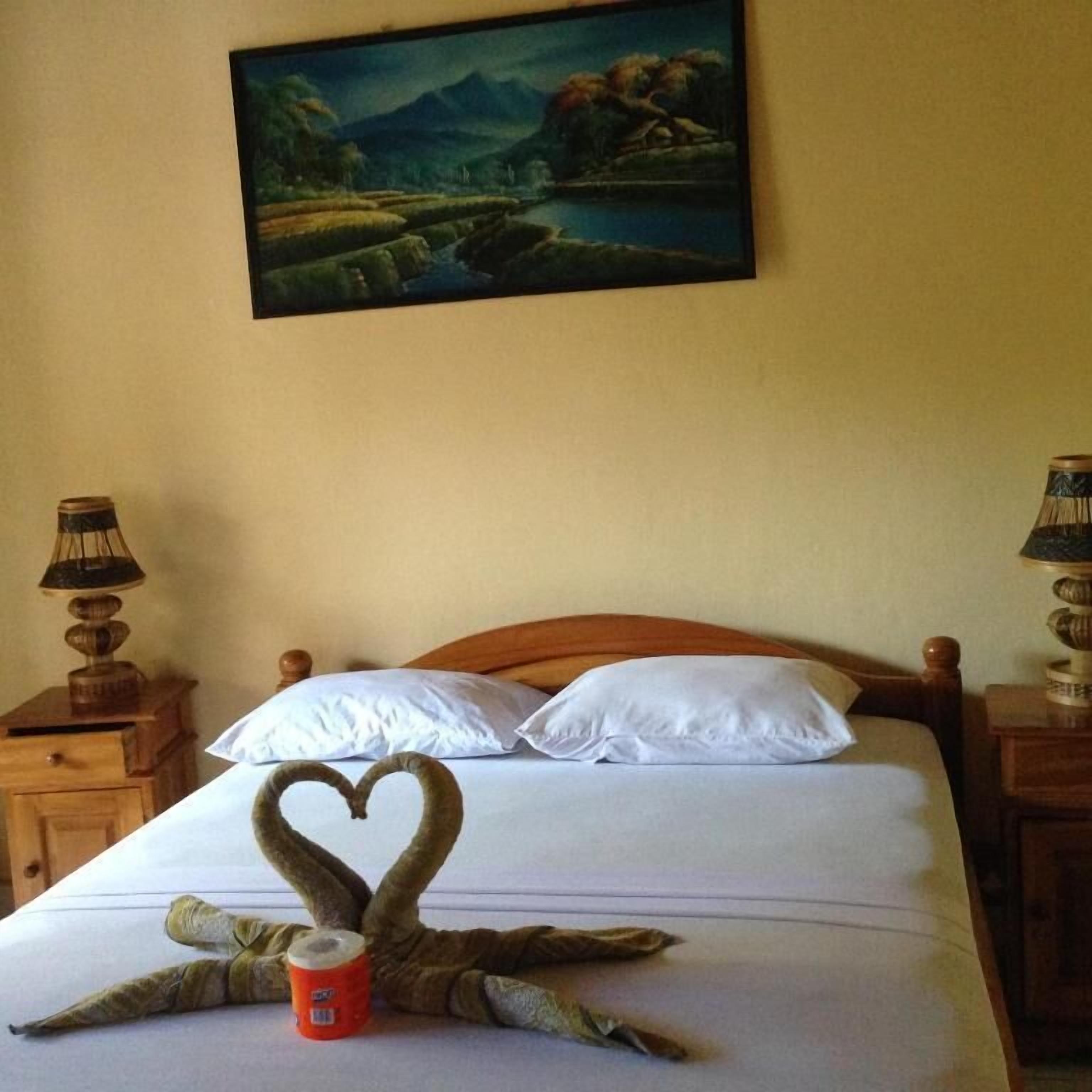 Ein Bett mit einer herzförmigen Handtuchgestaltung, ein Gemälde an der Wand und zwei Nachttischlampen.