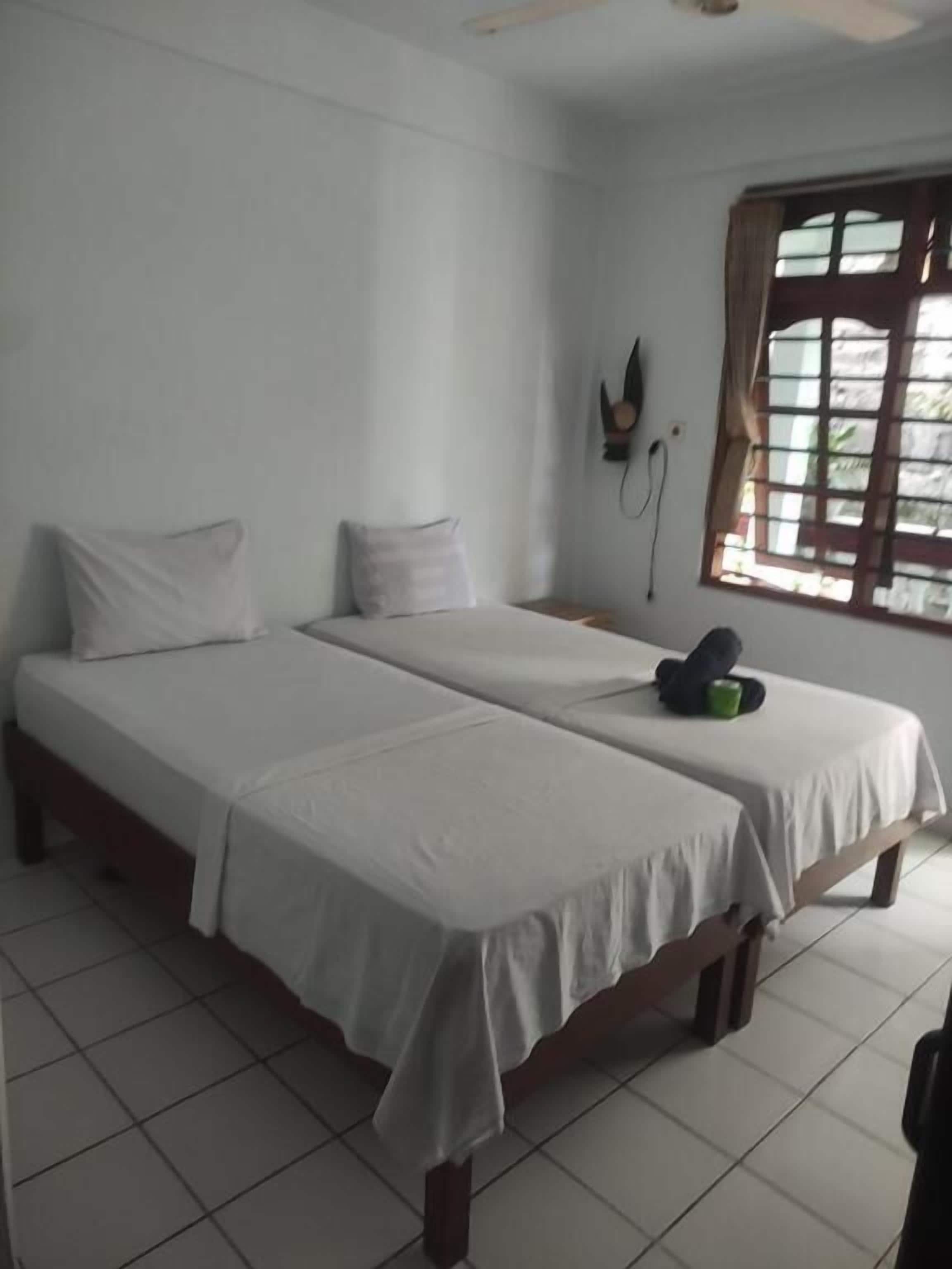 Una habitación con dos camas individuales, una ventana con cortinas y un televisor de pared.