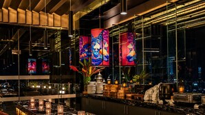 Een moderne bar met een lange toonbank, meerdere krukken en decoratieve elementen zoals kleurrijke panelen en kaarsen.