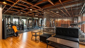 Een sportschool met houten vloer, fitnessapparatuur en een zithoek met een bank en tafel.