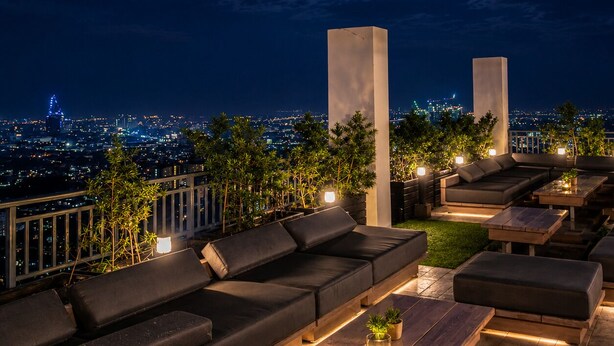 Een terras met loungemeubels, zoals banken en tafels, met uitzicht op de stad en een maan aan de hemel.