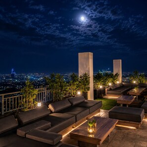 An outdoor lounge area with sofas and tables, a city view, and a moon in the sky. - Cozy 1BR Condo Near IT and Ayala can accommodate up to 6 pax by Benj's Place (Cebu City)