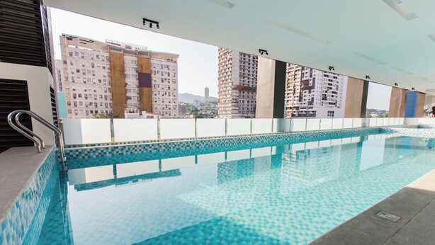 A swimming pool with a tiled pattern, a metal handrail, and a view of high-rise buildings in the background. - Cozy 1-bedroom condo, Wifi, Pool, Netflix, near IT Park (Cebu City)
