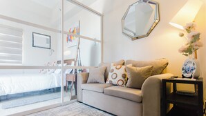 A modern room with a sofa, a side table, a mirror, and a window with blinds. - Cozy 1-bedroom condo, Wifi, Pool, Netflix, near IT Park (Cebu City)