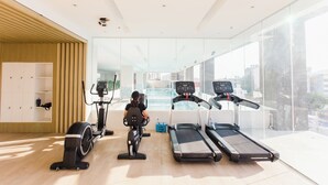 A modern gym with exercise equipment, large windows, and a view of the city. - Cozy 1-bedroom condo, Wifi, Pool, Netflix, near IT Park (Cebu City)