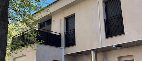 Un immeuble à plusieurs étages, doté d’une façade sobre, de grandes fenêtres avec volets et d’un balcon orné d’une rambarde en métal.