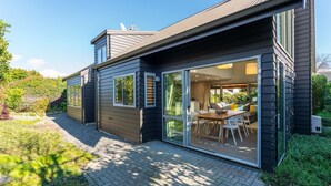 Une maison moderne dotée d’un patio, d’un coin repas avec une table et des chaises, et d’une grande porte-fenêtre coulissante donnant sur un espace intérieur.
